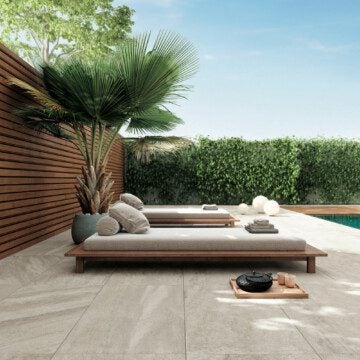 Two lounge beds poolside with a plant behind them and some throw pillows placed on the lounge beds