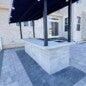 Outdoor kitchen installation with custom-built wood-burning grill, overhead cedar beams, stone fire pit, integrated bench seating, and happy client enjoying the finished space.