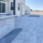 Outdoor kitchen installation with custom-built wood-burning grill, overhead cedar beams, stone fire pit, integrated bench seating, and happy client enjoying the finished space.