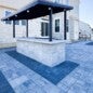 Outdoor kitchen installation with custom-built wood-burning grill, overhead cedar beams, stone fire pit, integrated bench seating, and happy client enjoying the finished space.
