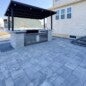 Outdoor kitchen installation with custom-built wood-burning grill, overhead cedar beams, stone fire pit, integrated bench seating, and happy client enjoying the finished space.