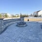 Outdoor kitchen installation with custom-built wood-burning grill, overhead cedar beams, stone fire pit, integrated bench seating, and happy client enjoying the finished space.